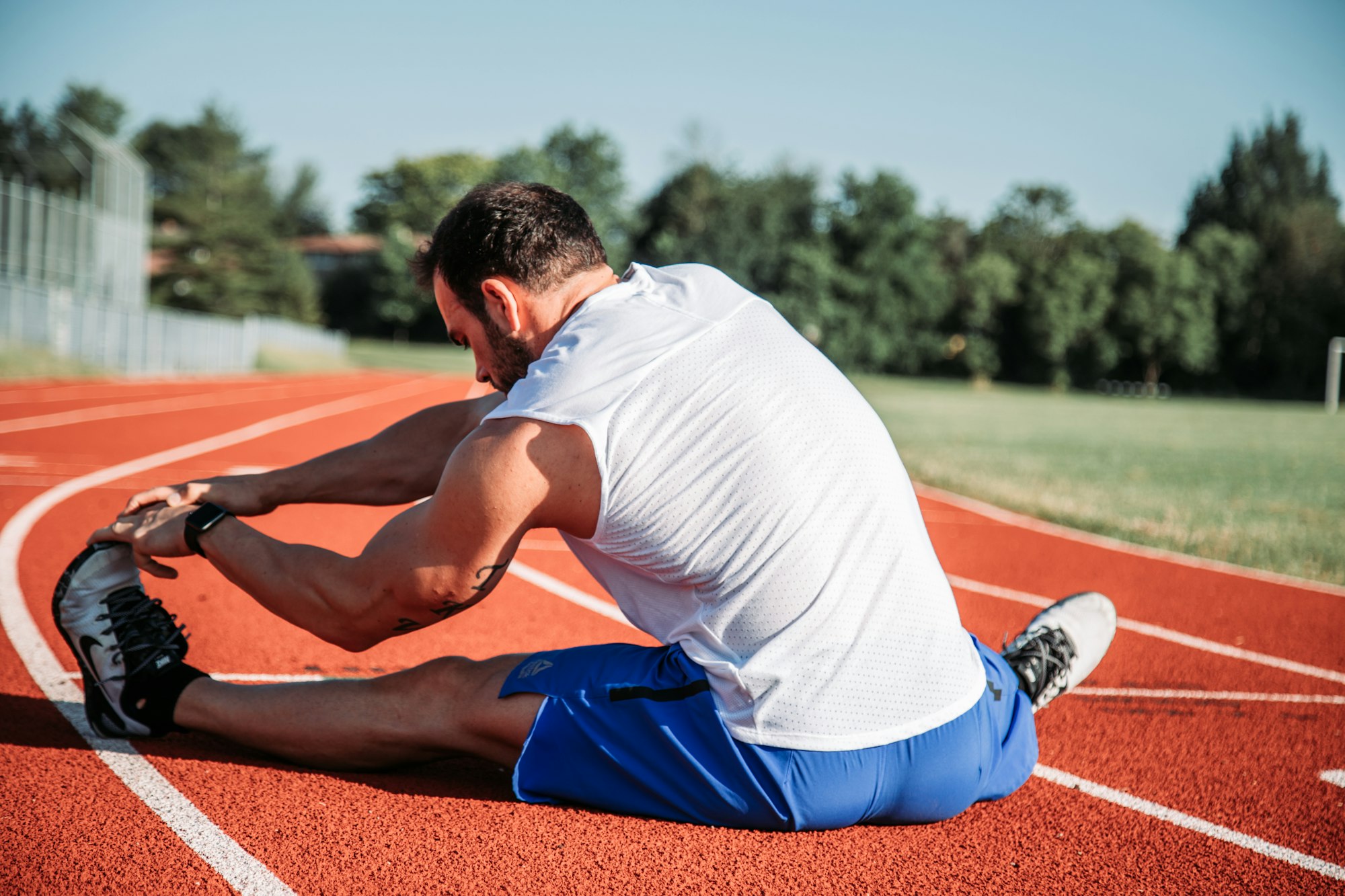 Endurance athlete stretching hamstrings on a red running track