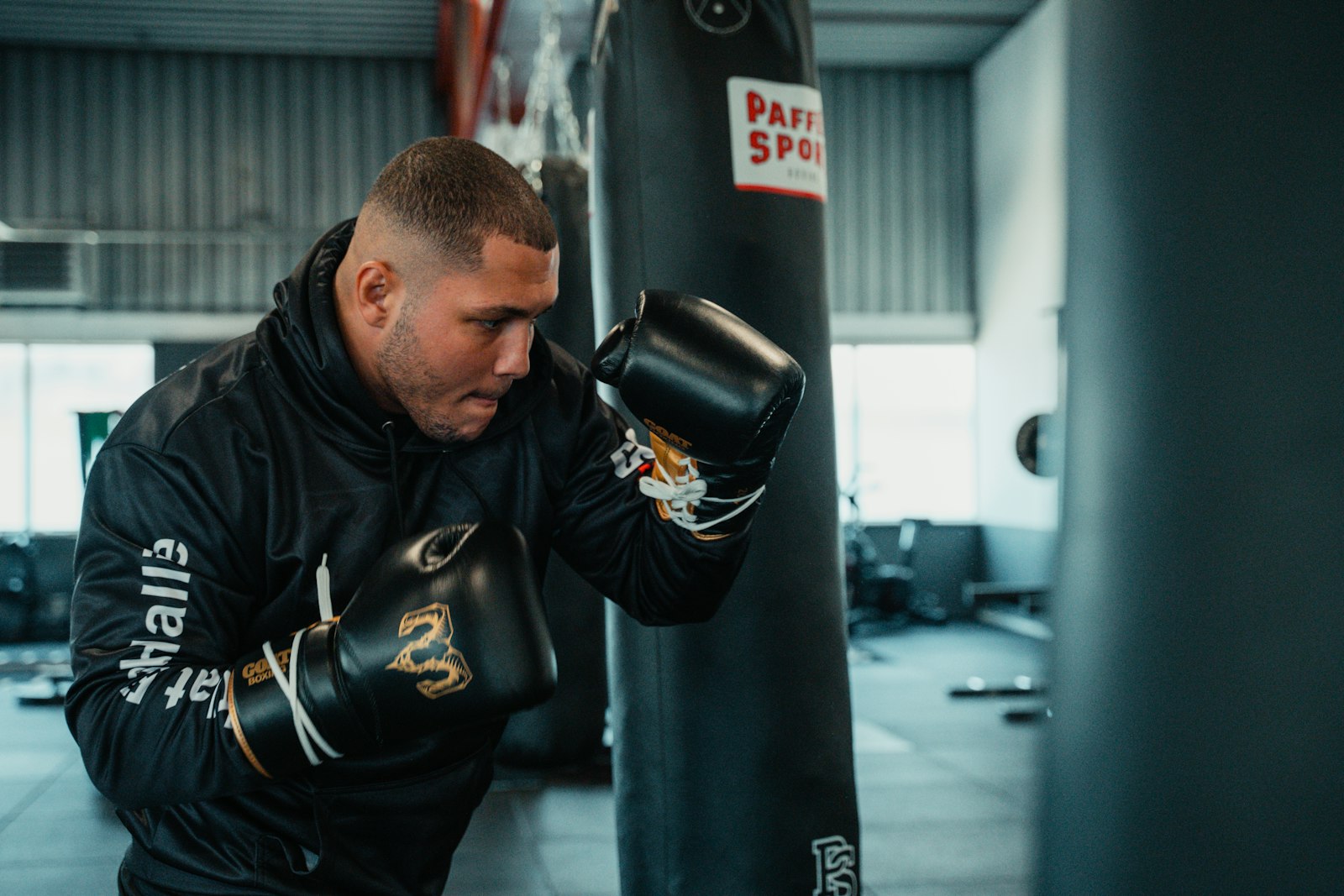 A boxer in a black hoodie strikes a heavy bag during a gym training session