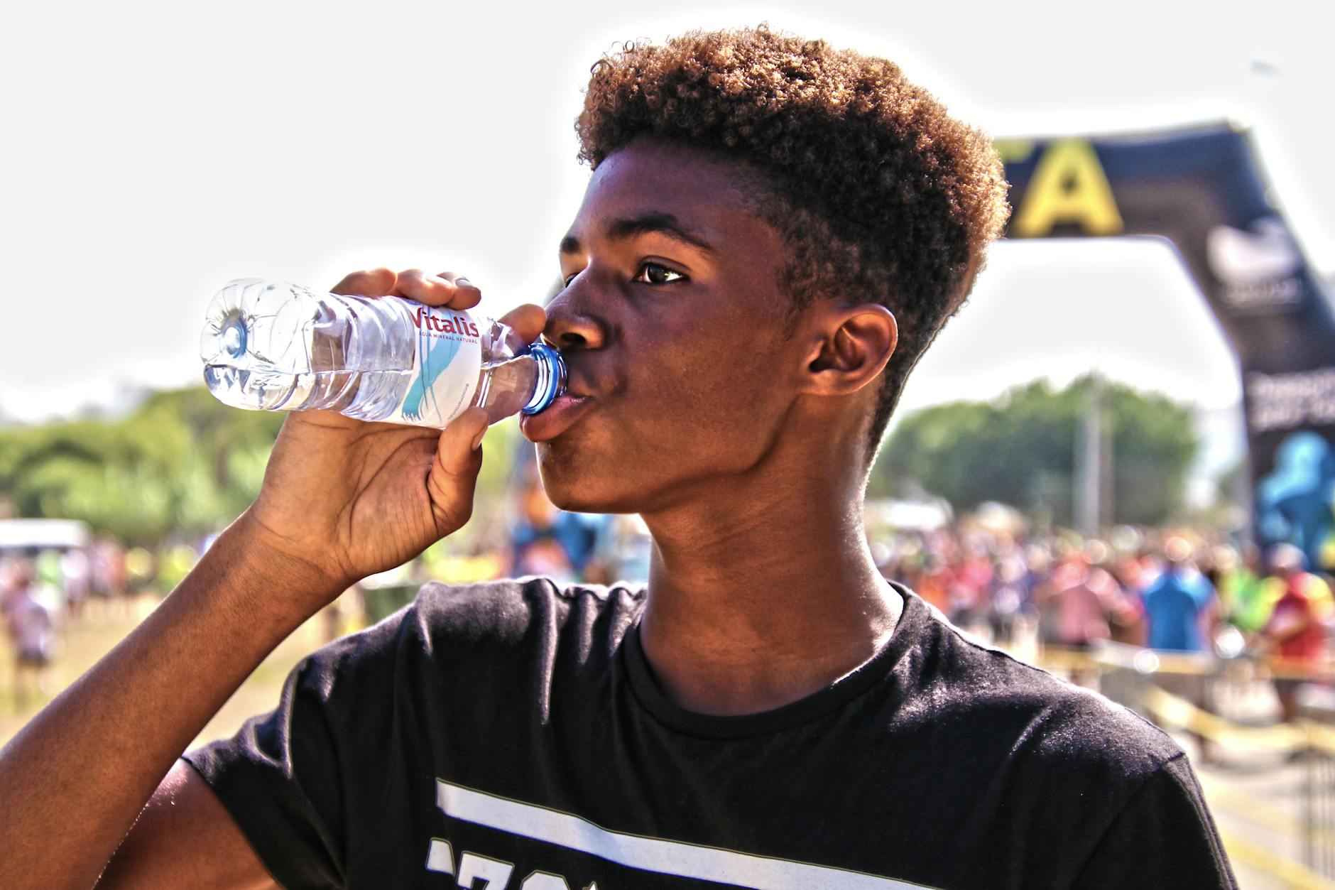 A young man drinking bottled water outdoors at a sporting event, showcasing hydration and fitness.
