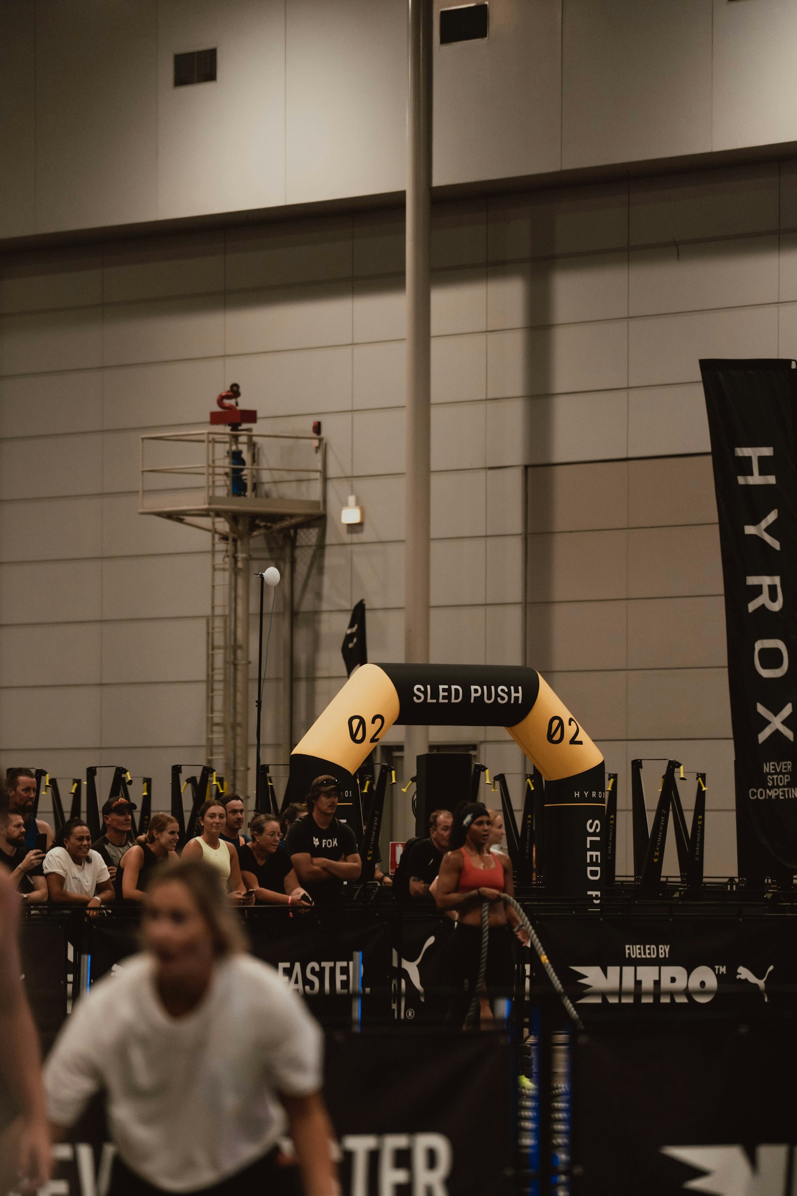 Athlete pushing a weighted sled at an indoor Hyrox fitness competition — illustrating the hydration demands of the 8-run, 8-station race format.