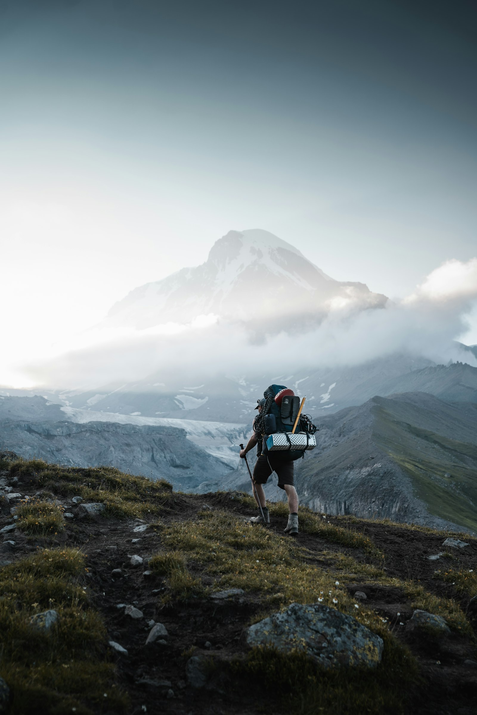 Hiker carrying a backpack climbing a sunlit mountain trail in summer, illustrating backcountry hydration needs