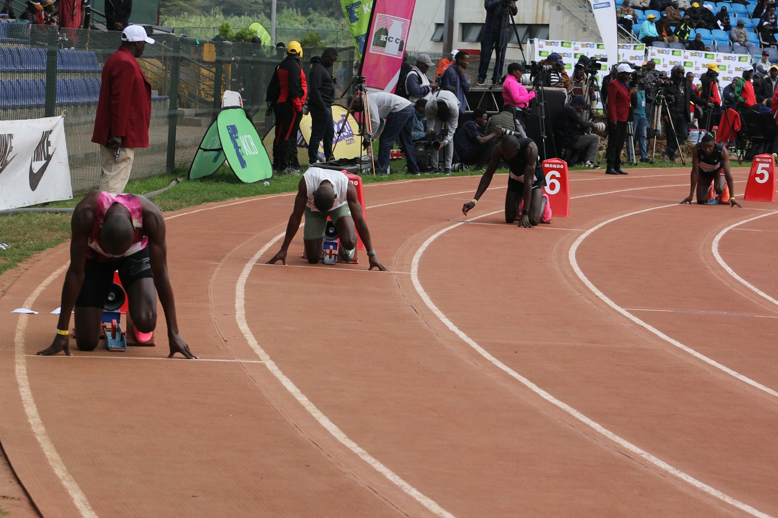 Sprinters settling into starting blocks at an outdoor track meet — illustrating the long, sun-exposed meet days behind track and field hydration demands.