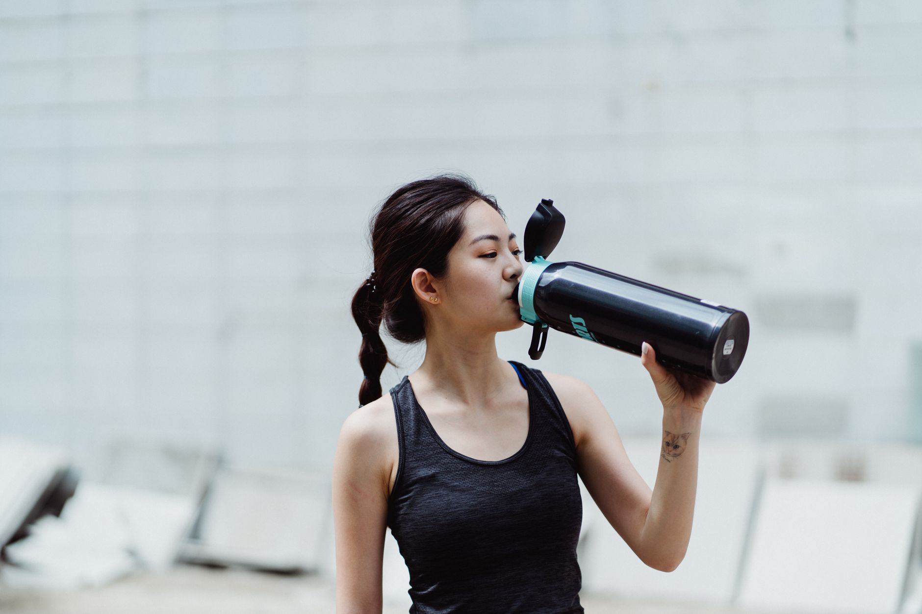Young woman in workout attire drinks from a water bottle, promoting healthy lifestyle.
