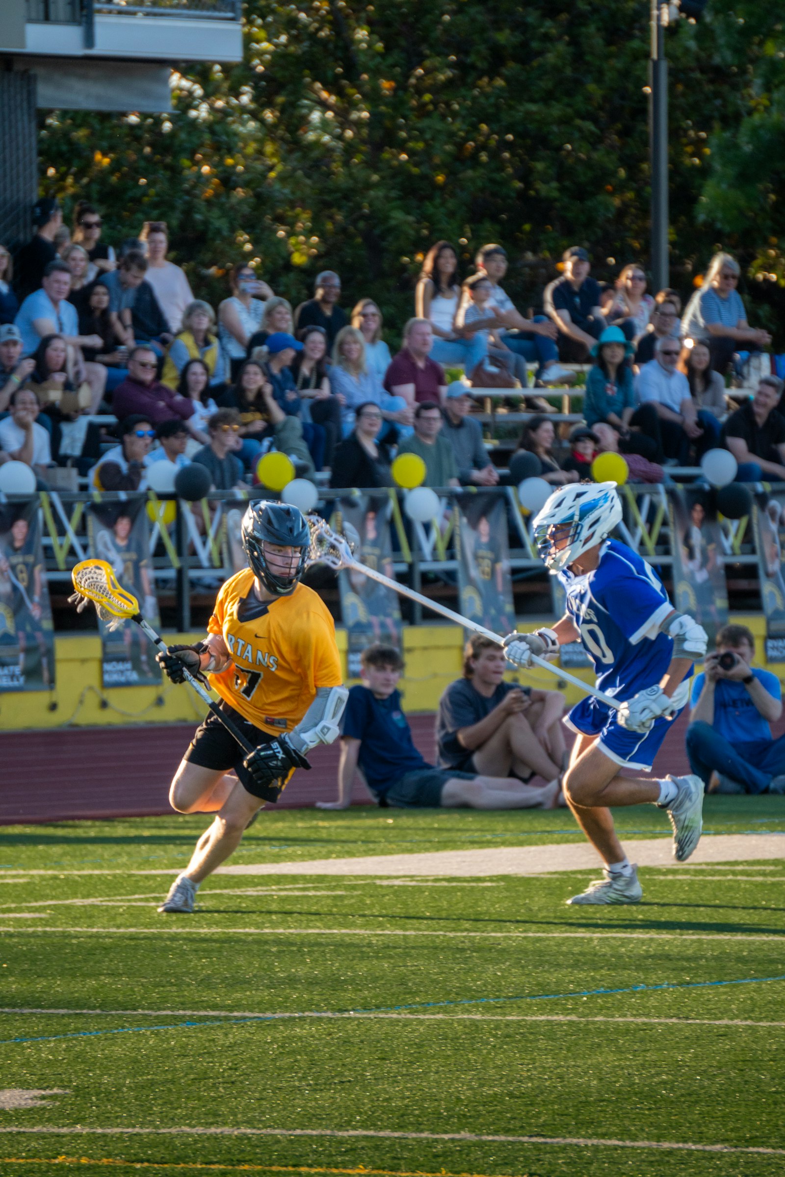 Lacrosse players competing on a field with a crowd behind them — illustrating the high sweat rates and hydration demands of lacrosse.