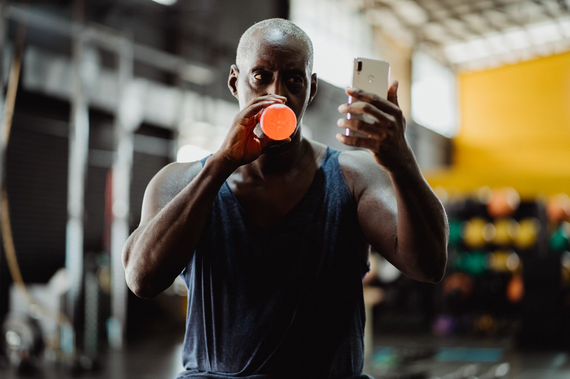 Athletic man drinking while checking smartphone in a modern gym environment.