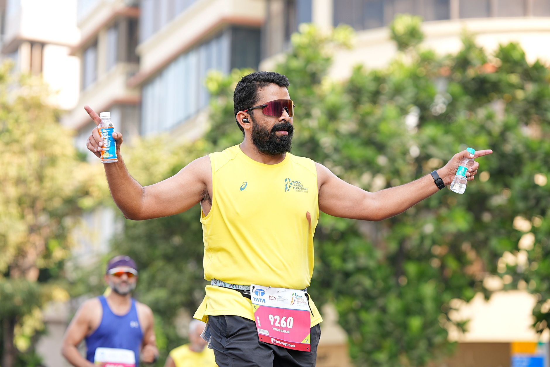 Male runner in a marathon holding drinks, wearing a yellow shirt, outdoors.