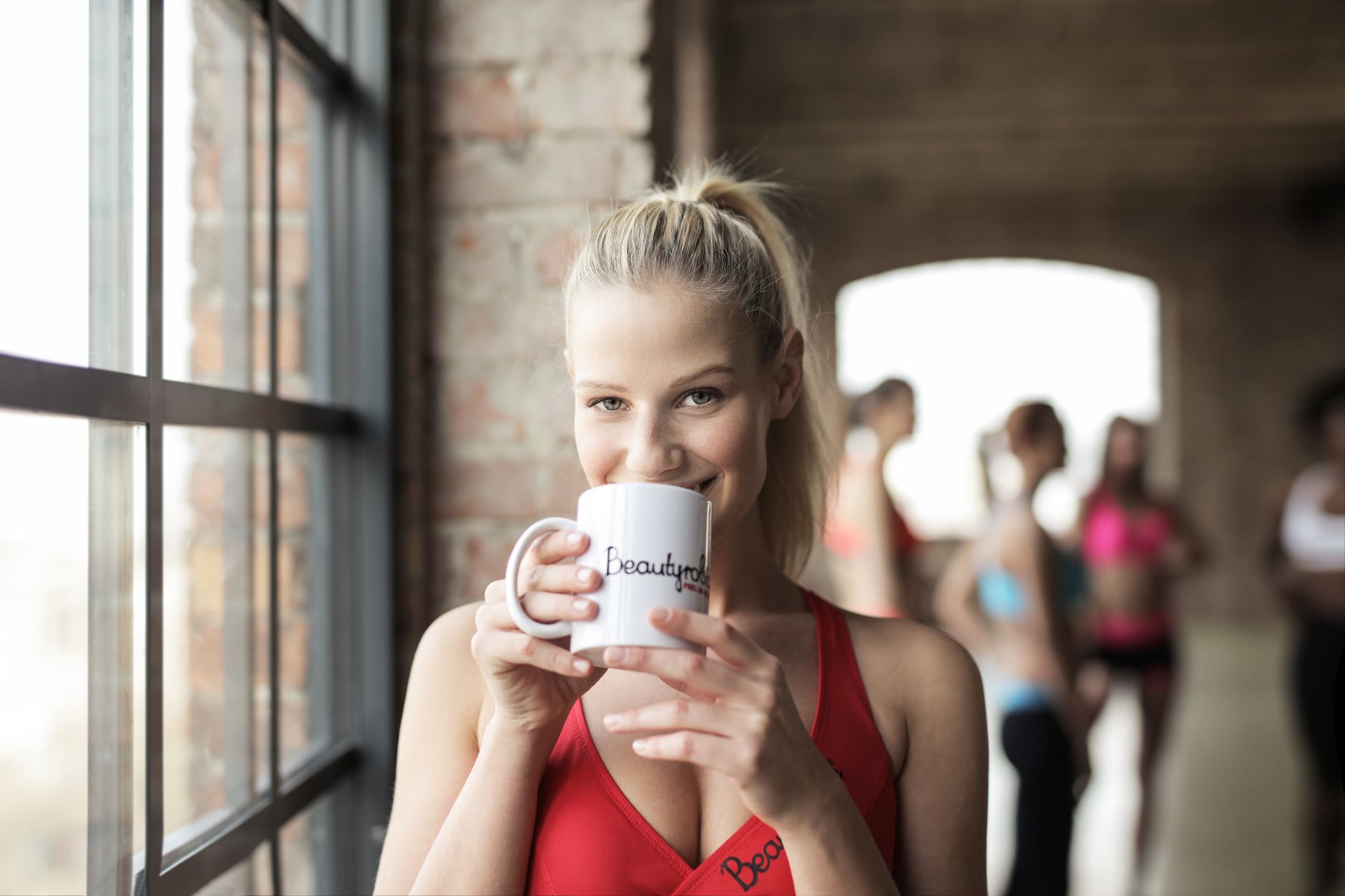 Blonde woman holding a mug, smiling during a fitness session indoors.