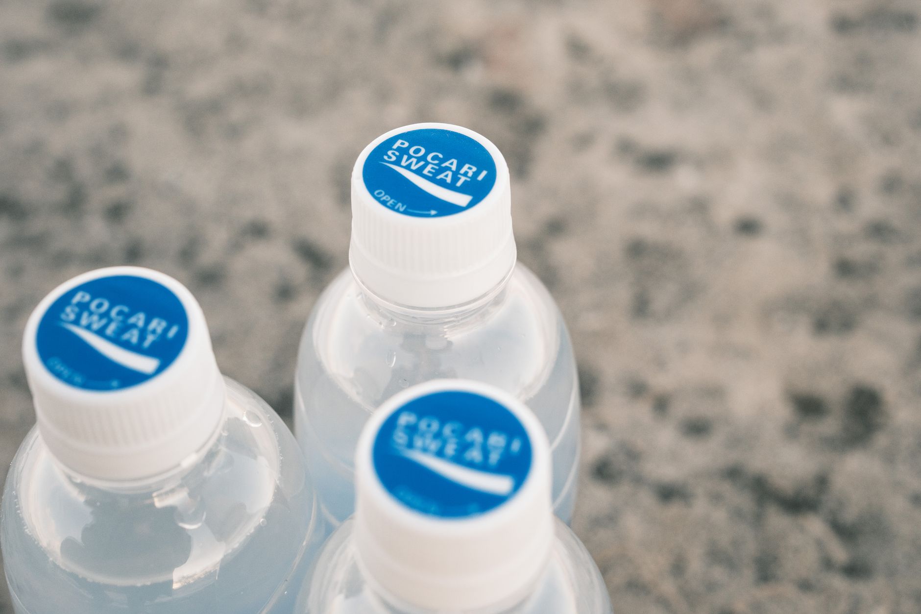 Three Pocari Sweat bottles on a stone surface, focus on blue caps.