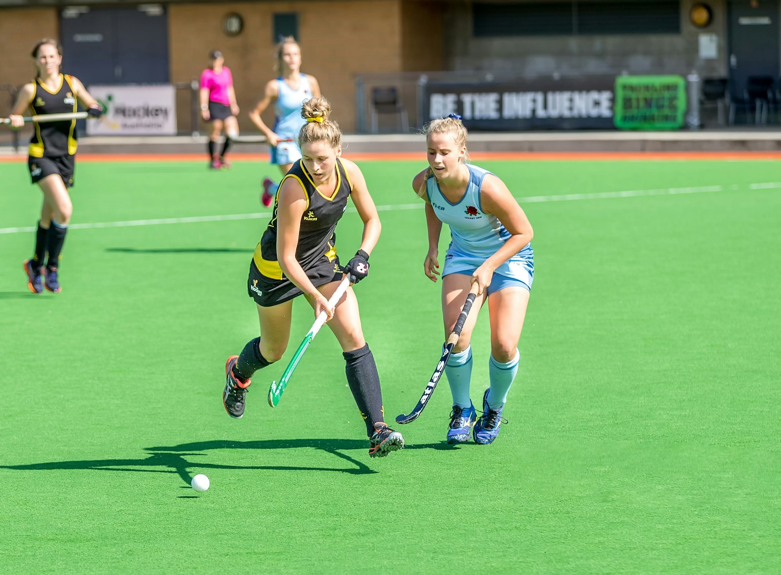 Two female field hockey players competing on green synthetic turf during a national championship match — illustrating the hydration demands of field hockey in summer preseason.