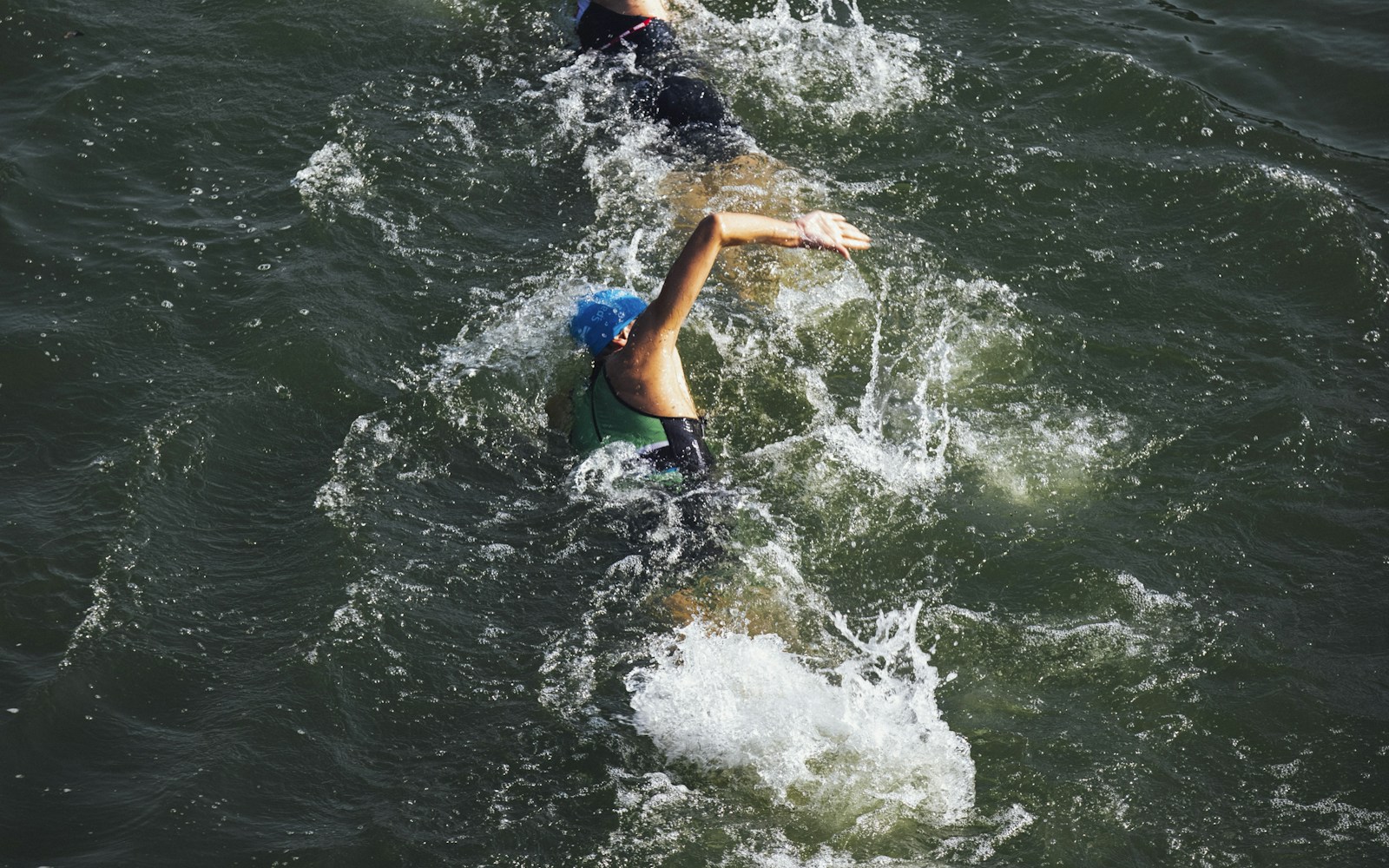 Group of athletes swimming in open water at an Ironman triathlon race start — illustrating the hydration demands of a 140.6-mile long-course race.