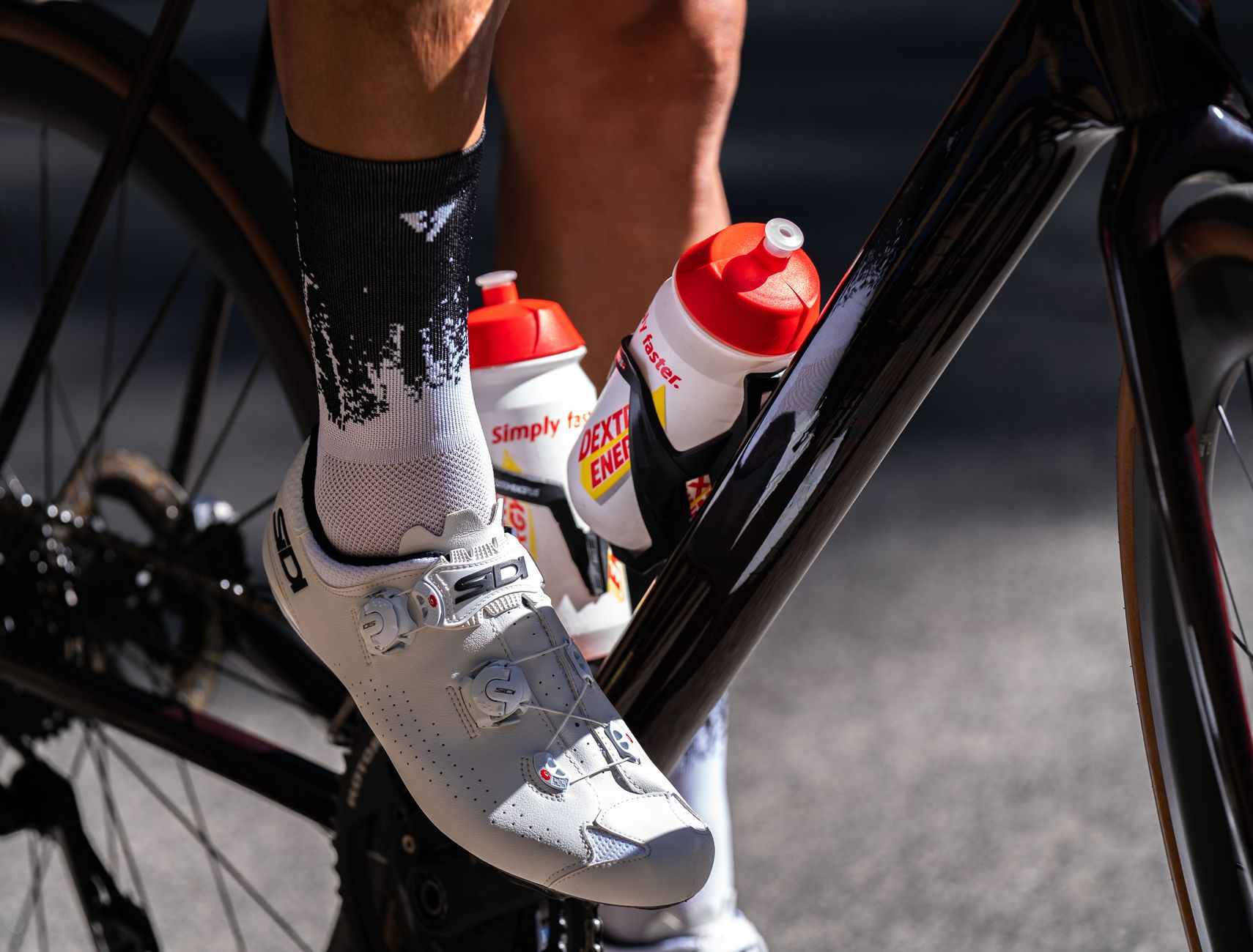 Cyclist's shoe on pedal with energy drink bottles attached to bike frame.