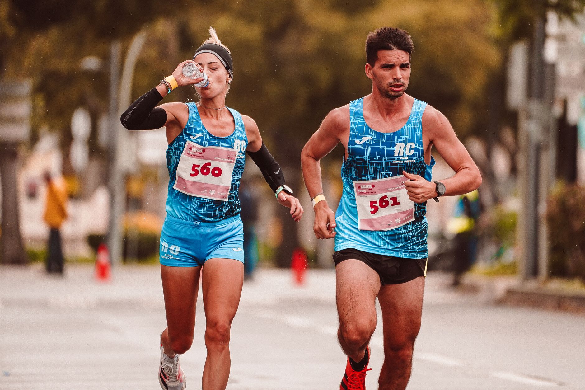 Two athletes participating in a marathon, hydrating and focused, while running outdoors on a city street.